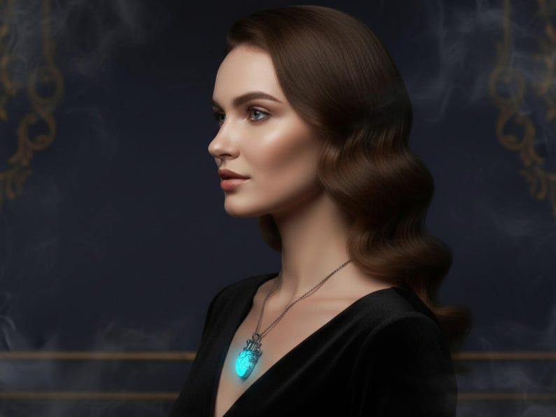 Puede incluir: Una mujer con un vestido negro y un collar plateado con un colgante azul brillante. El colgante tiene forma de coraz&oacute;n con detalles intrincados. La mujer tiene cabello casta&ntilde;o y mira hacia un lado.