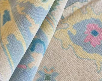 May include: Rolled-up patterned rug featuring a pastel colour scheme. The rug has a light blue, yellow, and pink floral design on a neutral background. The surface is textured, and the pattern is detailed.