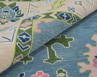 Könnte beinhalten: Nahaufnahme eines aufgerollten Teppichs mit blau-beigem Farbschema. Der Teppich hat ein detailliertes Blumenmuster mit grünen, rosa und blauen Akzenten. Das Design umfasst geometrische Formen und stilisierte Blumenmotive.