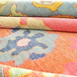 May include: Close-up of a rolled-up rug with a colorful, intricate pattern. The rug features a mix of coral, blue, yellow, and green hues. The design includes floral and geometric shapes, creating a textured and layered appearance.