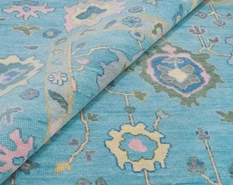 Könnte beinhalten: Türkisfarbener Teppich mit floralem Muster in Rosa, Gelb und Blau. Der Teppich ist gefaltet und zeigt die Unterseite. Das Design zeigt stilisierte Blumen und Blätter und schafft ein dekoratives Textil.