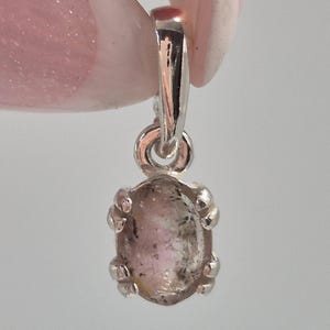 Peut inclure: Un pendentif en argent avec une pierre translucide de forme ovale présentant des inclusions roses et grises. La pierre est maintenue par un sertissage à quatre griffes avec une bélière en argent poli sur le dessus pour une chaîne.