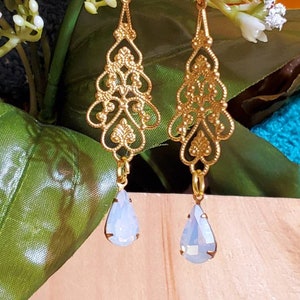 May include: Gold filigree dangle earrings with teardrop-shaped iridescent white glass stones.