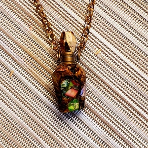 May include: A gold chain necklace with a clear glass bottle pendant. The bottle is filled with iridescent green, pink, and brown pieces of seashells.