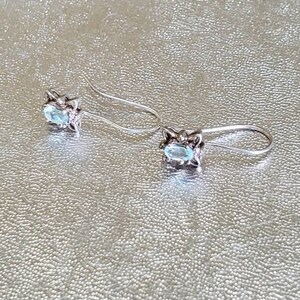 May include: A pair of silver dangle earrings with light blue oval-shaped gemstones set in a floral design.