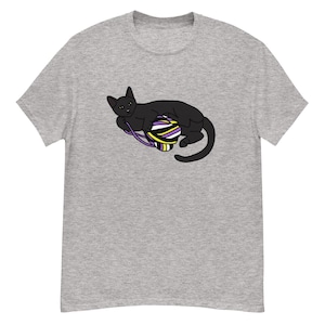 Op de afbeelding: Lichtgrijs t-shirt met een zwarte kat die speelt met een bol garen. De bol garen heeft paarse, gele en witte strepen. De kat ligt met zijn staart opgerold.