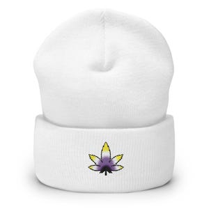 Könnte beinhalten: Ein weißer Beanie mit einem nicht-binären Cannabisblatt-Design. Das Blatt ist mit gelben, lila und schwarzen Farben bestickt. Der Beanie besteht aus einem weichen, gestrickten Material, ideal für kühles Wetter.