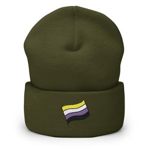 Könnte beinhalten: Olivgrüne Beanie-Mütze mit umgeschlagenem Saum. Die Mütze hat eine gestickte nicht-binäre Pride-Flagge in Gelb, Weiß, Lila und Schwarz. Ein modisches Accessoire, um Identität auszudrücken und Inklusion zu unterstützen.