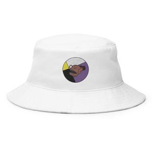 May include: White bucket hat with an embroidered circular design. The design features a brown, toothy creature within a segmented circle of yellow, black, and purple. The hat is made of a soft, durable fabric and has a wide brim.