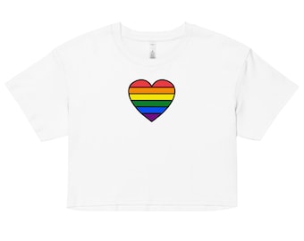 Può includere: Top corto bianco con un design a cuore arcobaleno. Il cuore presenta strisce orizzontali rosse, arancioni, gialle, verdi, blu e viola, delineate in nero. La maglietta ha maniche corte e girocollo.