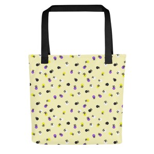 May include: A tote bag with a black handle and a light yellow background. The bag features a repeating pattern of black, white, purple, and yellow shapes. The bag is designed for carrying items.