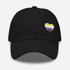 Könnte beinhalten: Schwarze Baseballkappe mit herzförmigem Aufnäher. Der Aufnäher zeigt ein Design der nicht-binären Pride-Flagge in Gelb, Weiß, Lila und Schwarz. Die Kappe hat einen gebogenen Schirm und einen Knopf oben.