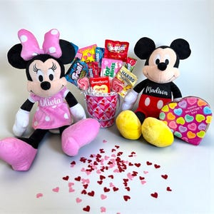 Puede incluir: Un set de regalo de San Valent&iacute;n con peluches de Minnie Mouse y Mickey Mouse. El set incluye una caja de caramelos en forma de coraz&oacute;n, un cubo de caramelos y confeti en forma de coraz&oacute;n esparcido. El peluche de Minnie Mouse lleva un vestido rosa con el nombre "Olivia".