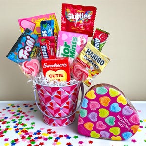 Puede incluir: Un ramo de caramelos de San Valent&iacute;n en un cubo rosa con un patr&oacute;n de corazones. El ramo incluye Skittles, Haribo Goldbears y piruletas en forma de coraz&oacute;n. Tambi&eacute;n hay una caja en forma de coraz&oacute;n con caramelos de coraz&oacute;n.
