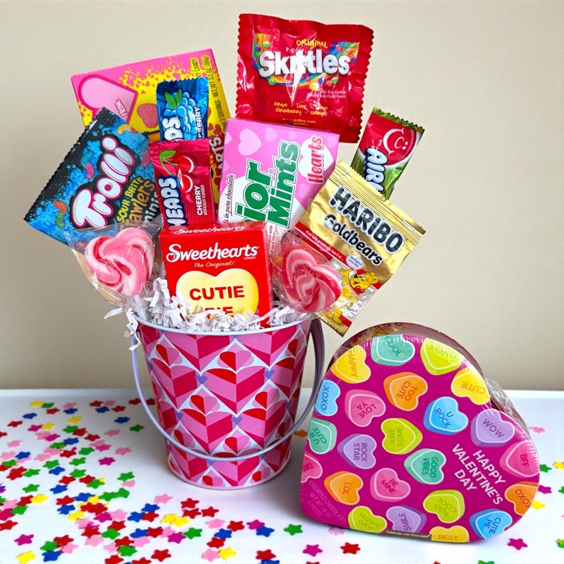 Puede incluir: Un ramo de caramelos de San Valent&iacute;n en un cubo rosa con un patr&oacute;n de corazones. El ramo incluye Skittles, Haribo Goldbears y piruletas en forma de coraz&oacute;n. Tambi&eacute;n hay una caja en forma de coraz&oacute;n con caramelos de coraz&oacute;n.