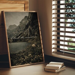 May include: A framed print featuring a sepia-toned landscape of mountains, a lake, and wildflowers. The text "Climb the mountain" is written across the image. The frame is made of wood.