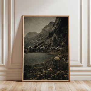 Puede incluir: Impresión enmarcada de un paisaje con una cordillera, un lago y flores silvestres. La imagen tiene una estética vintage con un tono sepia. El texto "Climb the mountain" está escrito en cursiva en la imagen.
