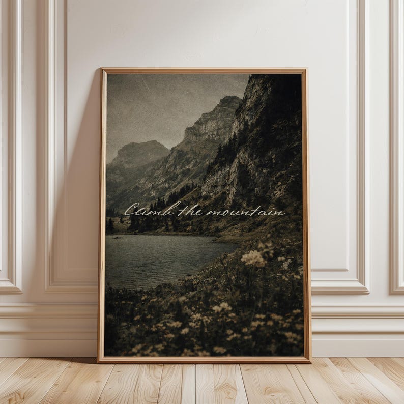 May include: Framed landscape print featuring a mountain range, lake, and wildflowers. The image has a vintage aesthetic with a sepia tone. The text "Climb the mountain" is written in a cursive font across the image.