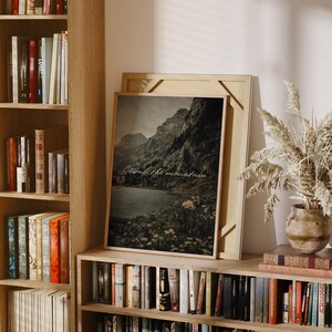 May include: A framed print featuring a grayscale mountain landscape with a lake and the text "Climb the mountain." The artwork is displayed on a wooden bookshelf, alongside other books and decorative items. The overall aesthetic is rustic and natural.