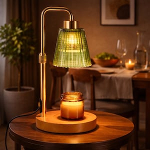 May include: A gold-toned table lamp with a green glass shade and a wooden base. A lit candle in a glass jar sits on the base. The lamp is on a dark wooden table, creating a warm, inviting ambiance.