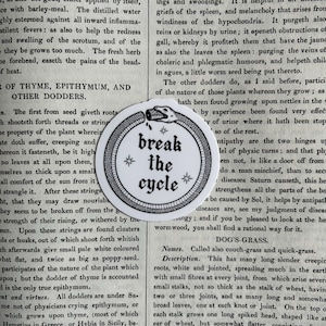 May include: A circular white sticker featuring a black line art illustration of an ouroboros snake eating its own tail. The center contains the black text "break the cycle" in a gothic font, accented by four small star symbols arranged around it.