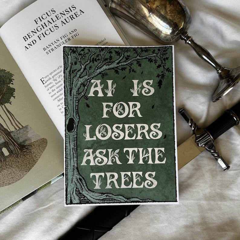 K&ouml;nnte beinhalten: Ein gr&uuml;ner und wei&szlig;er Kunstdruck mit dem Text "AI IS FOR LOSERS ASK THE TREES" wird angezeigt. Der Druck zeigt eine Baumillustration. Ein Buch und ein dekorativer Kelch sind ebenfalls sichtbar.