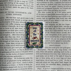 May include: A rectangular sticker featuring a decorative green and blue floral border surrounding the text "love the unloved" in blue lettering, accompanied by small illustrations of a bird, a mouse, and a frog, accented with gold stars.
