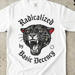 May include: A white short-sleeve t-shirt featuring a graphic of a snarling black panther head with red inner ears. The text "Radicalized by Basic Decency" is printed in a black gothic font around the panther. The logo "SEW SAD CO." is in the corner.