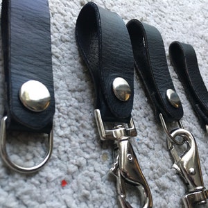 Pode incluir: Quatro chaveiros de couro preto com argolas e fechos de metal prateado. Os chaveiros t&ecirc;m um bot&atilde;o de metal prateado na tira de couro.