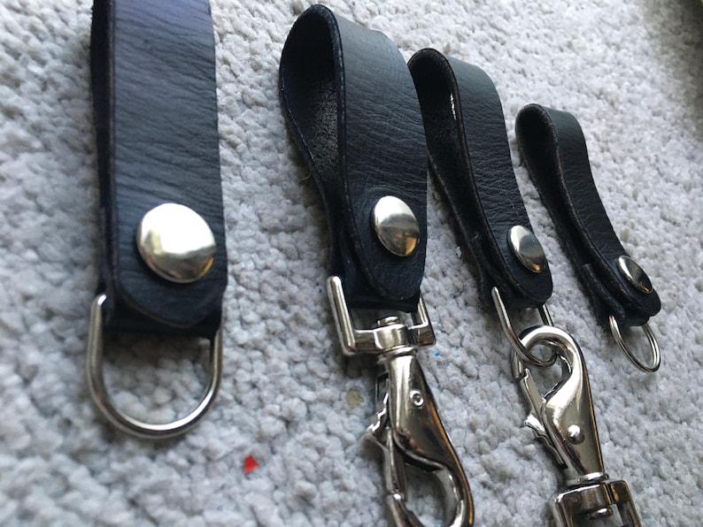 Pode incluir: Quatro chaveiros de couro preto com argolas e fechos de metal prateado. Os chaveiros t&ecirc;m um bot&atilde;o de metal prateado na tira de couro.