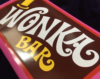 以下が含まれることがあります： ピンクと赤の箱で、茶色の背景に白い文字で「Wonka Bar」と書いてあり、黄色のシルクハットのグラフィックが描かれています。