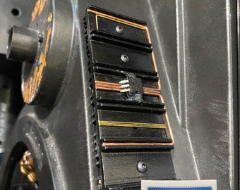 May include: Close-up of a black metal component with a copper wire and a series of black rectangular slots. The component is mounted on a gray metal surface. A sticker with the text "SR DESIGN CREATIONS" is visible in the lower right corner.