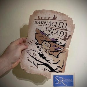 Puede incluir: Una ilustración marrón y blanca de un monstruo con el texto "Barnacled Dread" sobre un fondo parecido al pergamino. La ilustración es de estilo de dibujos animados y el monstruo tiene dientes afilados y un ojo grande y redondo. El texto "SR Design Creations" es visible en la esquina inferior derecha de la imagen.