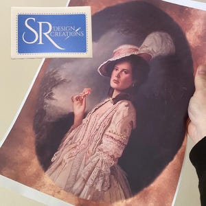 Könnte beinhalten: Druck eines Porträts einer Frau in rosa Kleid und Hut, die eine Blume hält. Das Kunstwerk hat eine Vintage-Ästhetik. Der Druck ist mit "SR DESIGN CREATIONS" auf einem blauen Aufkleber versehen.