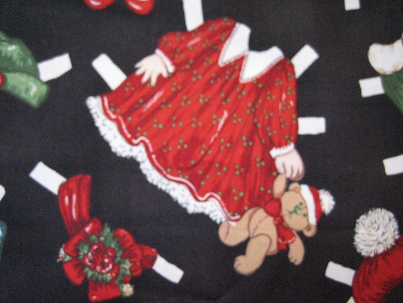 May include: A fabric pattern featuring Christmas-themed paper dolls on a black background. The dolls include a red dress with white lace trim, a teddy bear, and other festive elements. The design is whimsical and holiday-themed.