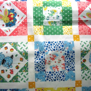 Op de afbeelding: Een patchworkquilt met vierkanten met verschillende patronen en afbeeldingen. De quilt toont een herhalend patroon van vierkanten met een gele konijn, een blauwe puppy en stippen in groen en blauw. De quilt is gemaakt van zachte stof.