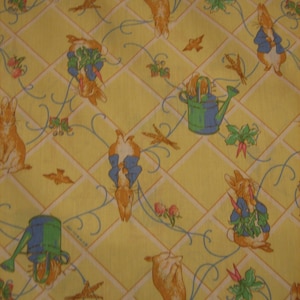 May include: A yellow fabric with a repeating pattern of bunnies, watering cans, and leafy plants. The bunnies are in various poses, including sitting, standing, and holding carrots. The watering cans are blue and green with a yellow handle.