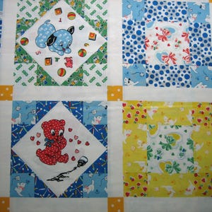 Op de afbeelding: Een patchworkquilt met een herhalend patroon van vierkanten. Elke vierkant heeft een ander ontwerp, waaronder een blauwe puppy, een rode teddybeer en bloemen- en stippenpatronen. De quilt is voornamelijk wit, blauw, geel en groen.