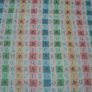 Puede incluir: Una tela colorida con un patrón repetitivo de letras del alfabeto, flores y pequeños animales. Las letras están en una fuente azul claro y están dispuestas en filas a través de la tela. Las flores son rosas y blancas y los animales son de varios colores.