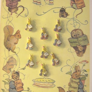 Puede incluir: Una colección de 10 botones de cerámica amarilla y blanca con personajes de Beatrix Potter. Los botones están dispuestos en dos filas sobre un fondo amarillo con ilustraciones de personajes de Beatrix Potter y escenas de sus libros.