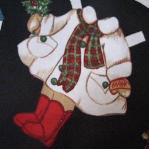 May include: A repeating pattern on a black background features cut-out figures of a winter coat, boots, and mittens. The coat is white with a red and green plaid scarf, green buttons, and a sprig of holly. Red boots and mittens complete the design.