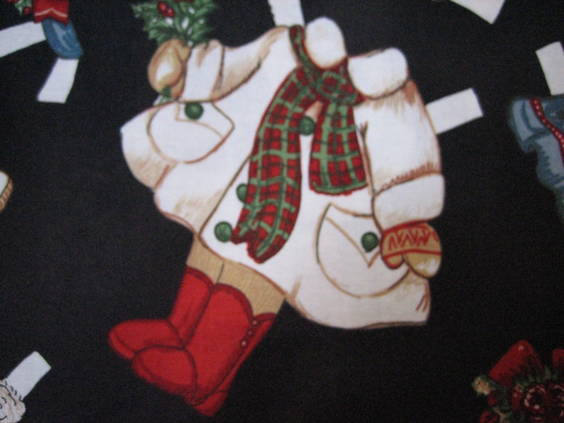 May include: A repeating pattern on a black background features cut-out figures of a winter coat, boots, and mittens. The coat is white with a red and green plaid scarf, green buttons, and a sprig of holly. Red boots and mittens complete the design.