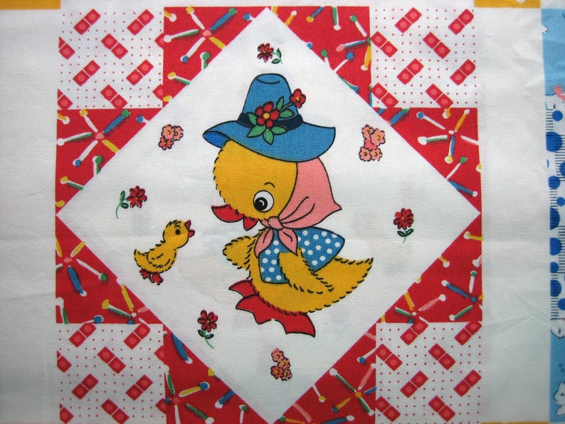 Op de afbeelding: Een vintage quiltblok met een gele eend met een blauwe hoed met rode bloemen en een roze sjaal. De eend is omgeven door rood-witte stof met een kleiner geel kuiken. De quilt heeft een witte achtergrond.