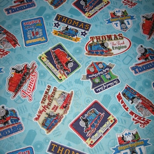 May include: Pale blue fabric patterned with Thomas the Tank Engine motifs. The design includes images of Thomas, James, and related text like "Thomas," "Really Useful," and "The Tank Engine." Suitable for children's projects.