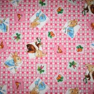 May include: A pink and white gingham fabric with illustrations of rabbits in blue jackets and brown coats, carrots, berries, and green sprigs. The fabric has a patchwork design.