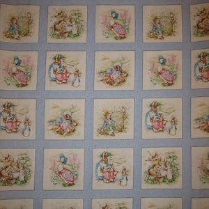 May include: A light blue fabric featuring a repeating grid pattern of square illustrations depicting Peter Rabbit characters. Each square contains scenes of rabbits and ducks in garden settings with soft watercolor tones of green, pink, and brown.