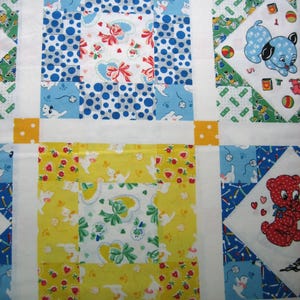 Op de afbeelding: Een patchworkquilt met een herhalend patroon van vierkanten. De vierkanten hebben verschillende ontwerpen, waaronder stippen, bloempatronen en cartoon dieren in tinten blauw, geel, groen en rood. Witte randen en gele stippen accenten maken het ontwerp compleet.