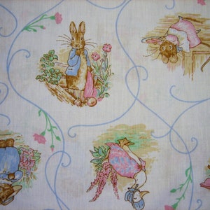 Puede incluir: Una tela blanca con un patrón repetido de personajes de Peter Rabbit. Los personajes incluyen Peter Rabbit, un conejo con una chaqueta azul, un ratón con un vestido rosa, un ganso y un conejo con una cesta. La tela tiene un fondo azul claro con un delicado patrón floral.