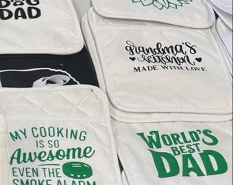 Peut inclure: Des maniques et maniques de cuisine blanches matelassées avec du texte et des graphiques verts et noirs. Les motifs incluent un tournesol, "Grandma's Kitchen", "My Cooking is Awesome" et "World's Best Dad."