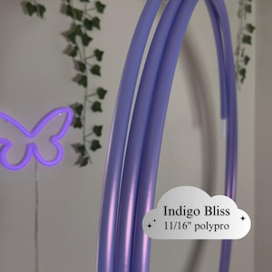 May include: A close-up of a lavender-colored hula hoop. The text "Indigo Bliss" and "11/16" polypro" is visible on a white cloud-shaped sticker. A neon purple butterfly is in the background.